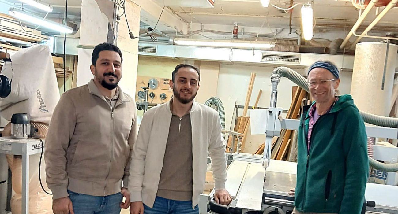 Amjed, Mahjed und Manfred stehen zusammen in der Holzwerkstatt.