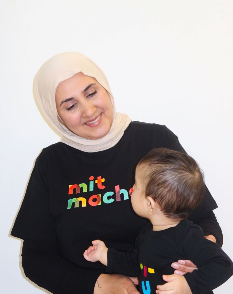 Jamile schaut liebevoll ihr Baby an, das sie auf dem Schoß hält.