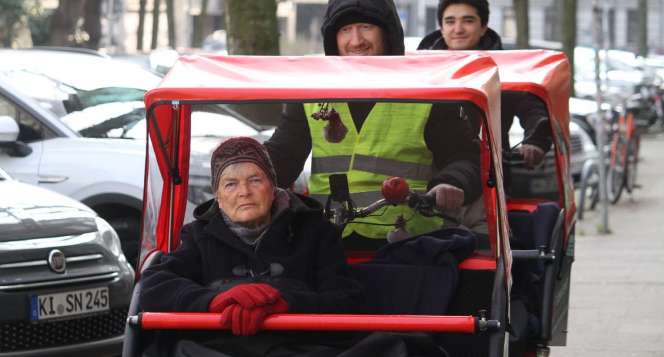 Eine Seniorin sitzt vorne in der fahrenden Rikscha.